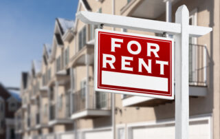 For Rent Real Estate Sign In Front of a Row of Apartment Condominiums Balconies and Garage Doors.